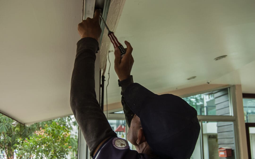 A technician is repairing a garage door mechanism using a screwdriver inside a residential building.
